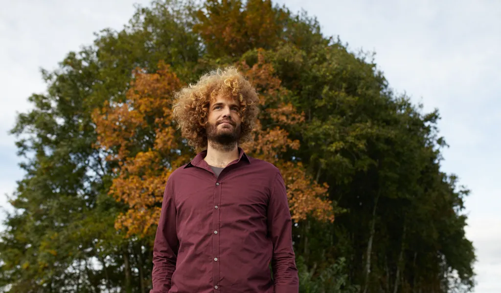 Niels Visser in het veld, voor een boom in herfstkleuren
